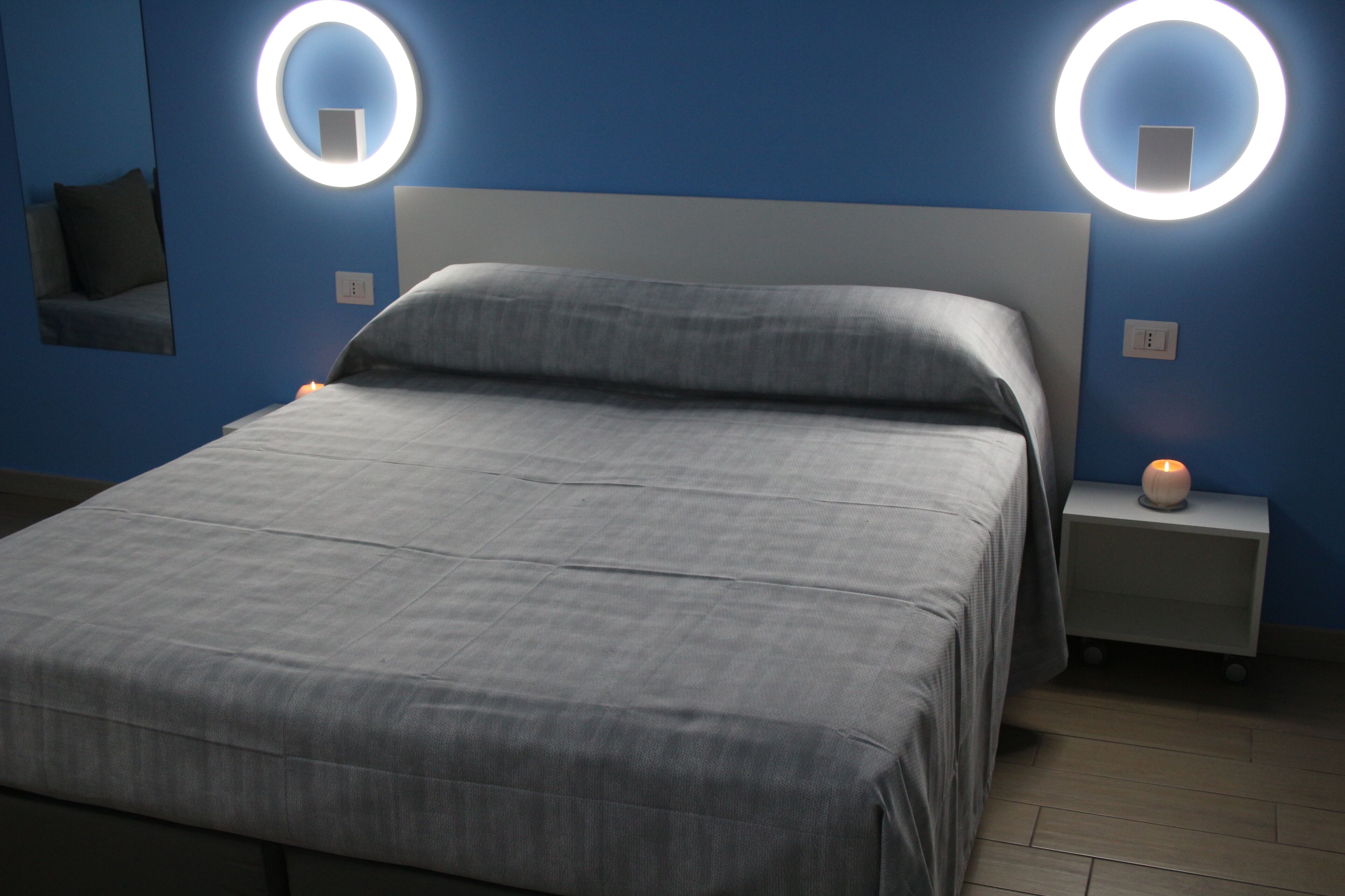 Une chambre moderne avec un grand lit, deux tables de chevet et des luminaires circulaires fixés au mur.