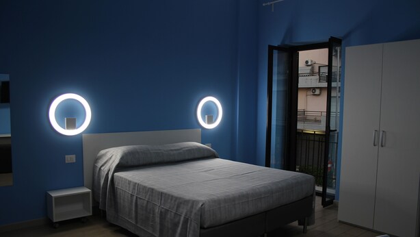 Ein Schlafzimmer mit einem Bett, Nachttischen, einem Kleiderschrank und einer runden Wandleuchte.