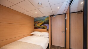 Een hotelkamer met een houten hoofdeinde, een bed met witte lakens, een schilderij aan de muur en een deur aan de rechterkant.
