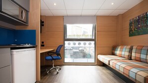 Een moderne kamer met een kitchenette, een blauwe bureaustoel, een bank met een ruitpatroon en een groot raam met uitzicht.