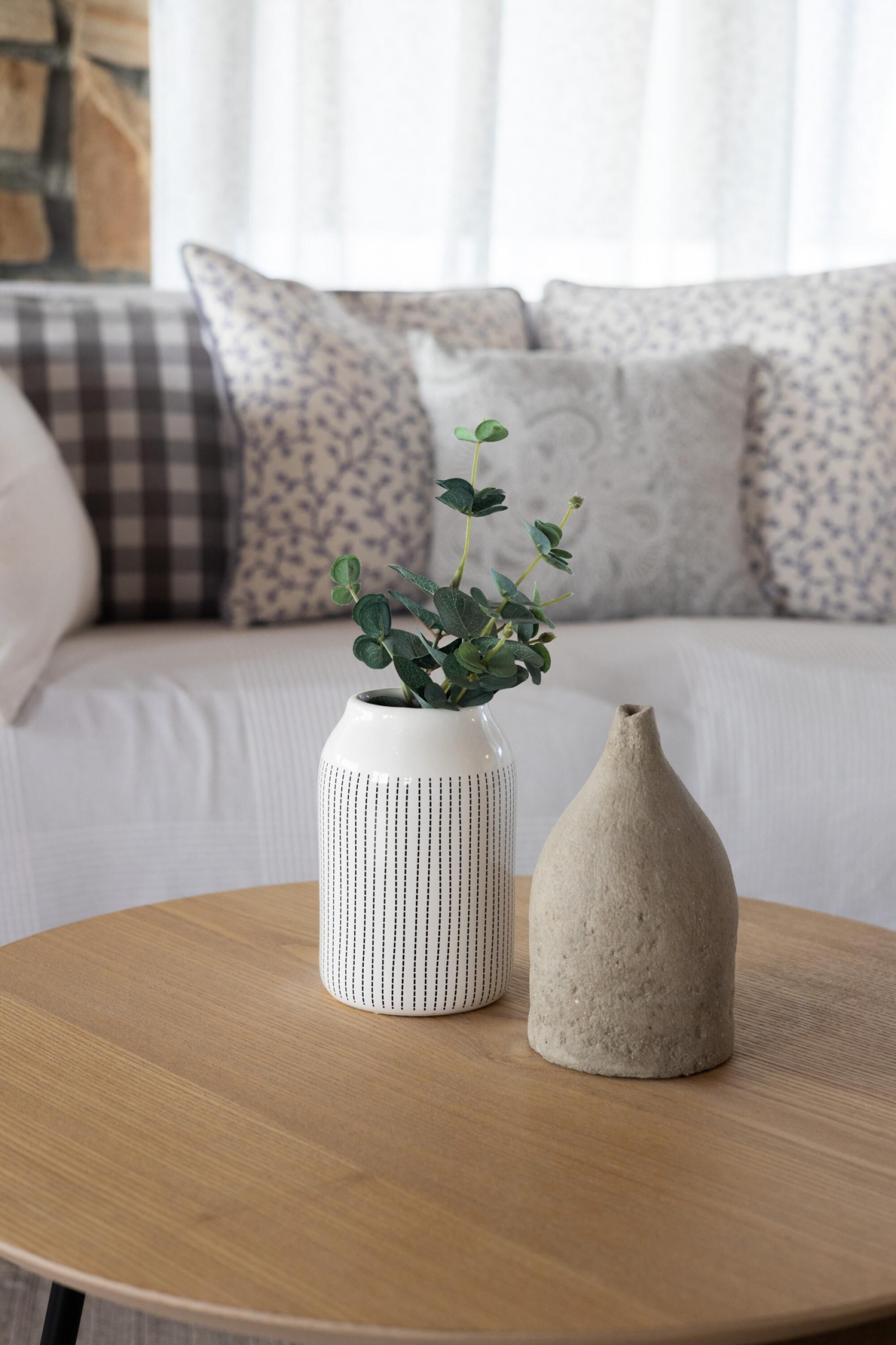 A round wooden table with two vases, one with a plant and another plain.