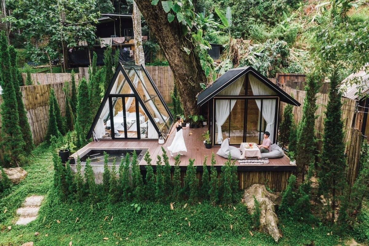 Un jardin doté d’une terrasse en bois, d’une structure recouverte d’une verrière et d’un petit bâtiment ressemblant à une maison, avec une table et des chaises.