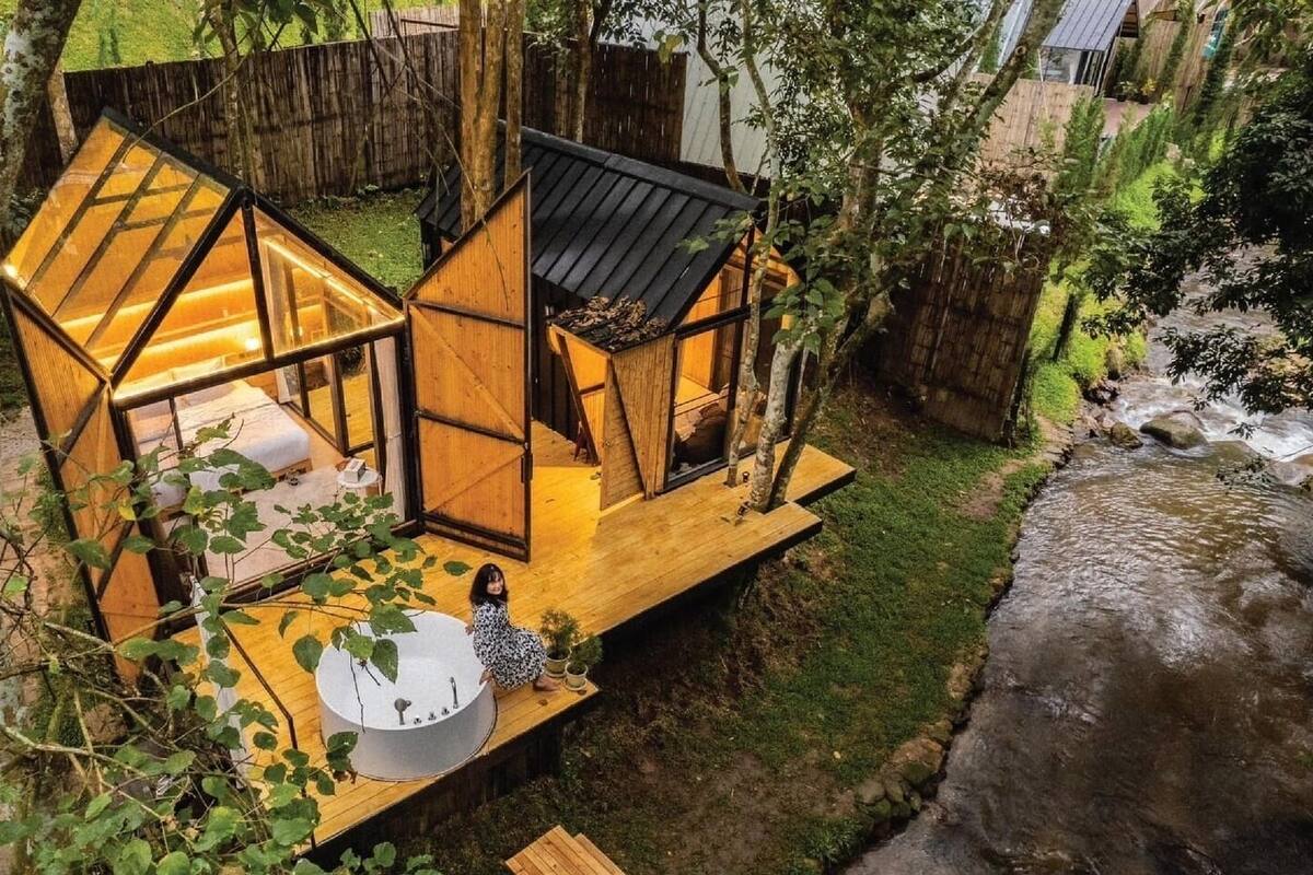 Une cabane dans les arbres dotée d’une terrasse en bois, d’un petit espace de détente extérieur et d’un élément décoratif aquatique.