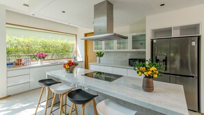 A modern kitchen with a large island, stainless steel appliances, and a view of greenery outside. - Enjoy A Luxurious 5 Bedroom Villa (Da Nang)