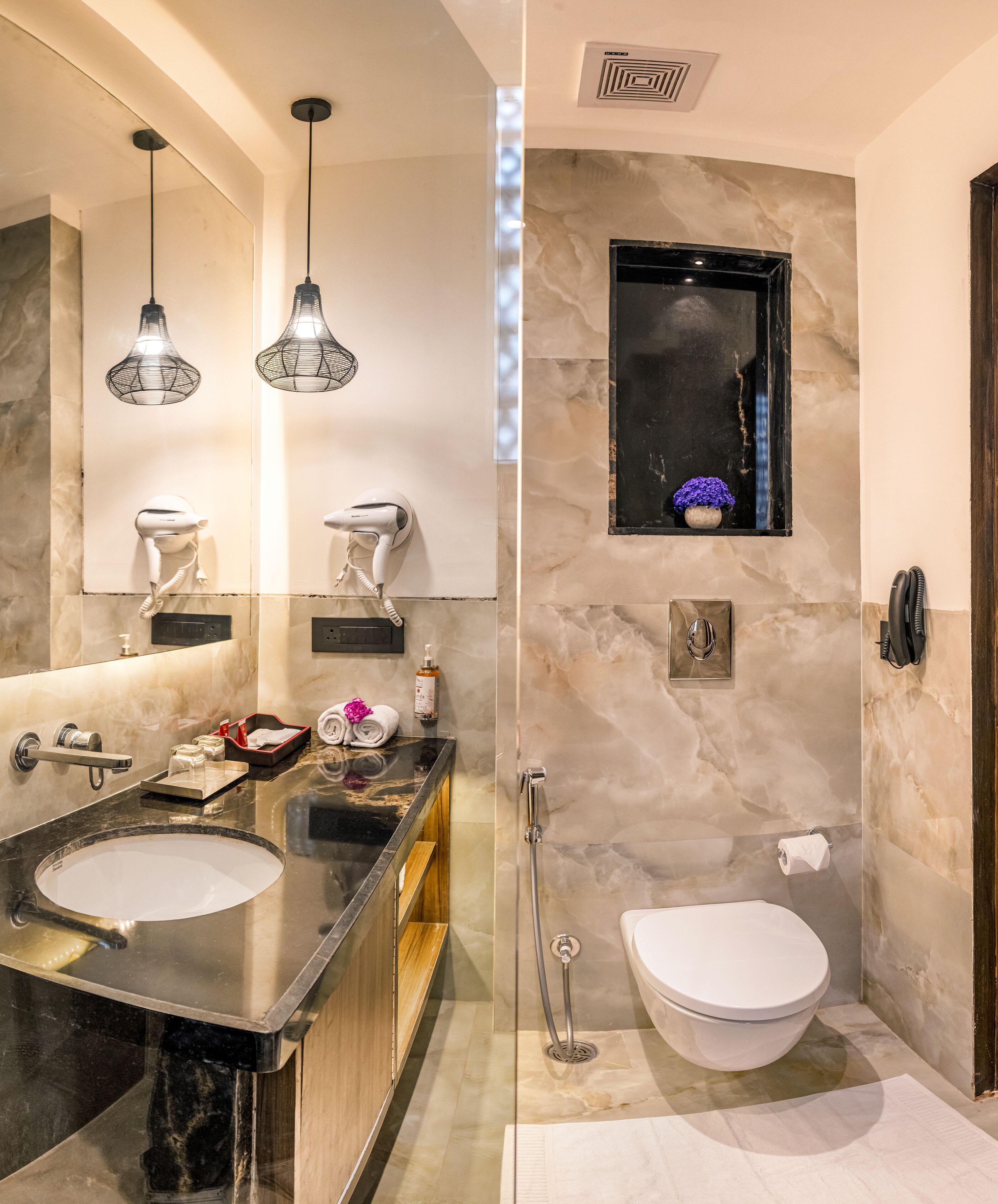 A modern bathroom with a large vanity, two hair dryers, a mirror, a small window with a flower, and a toilet.