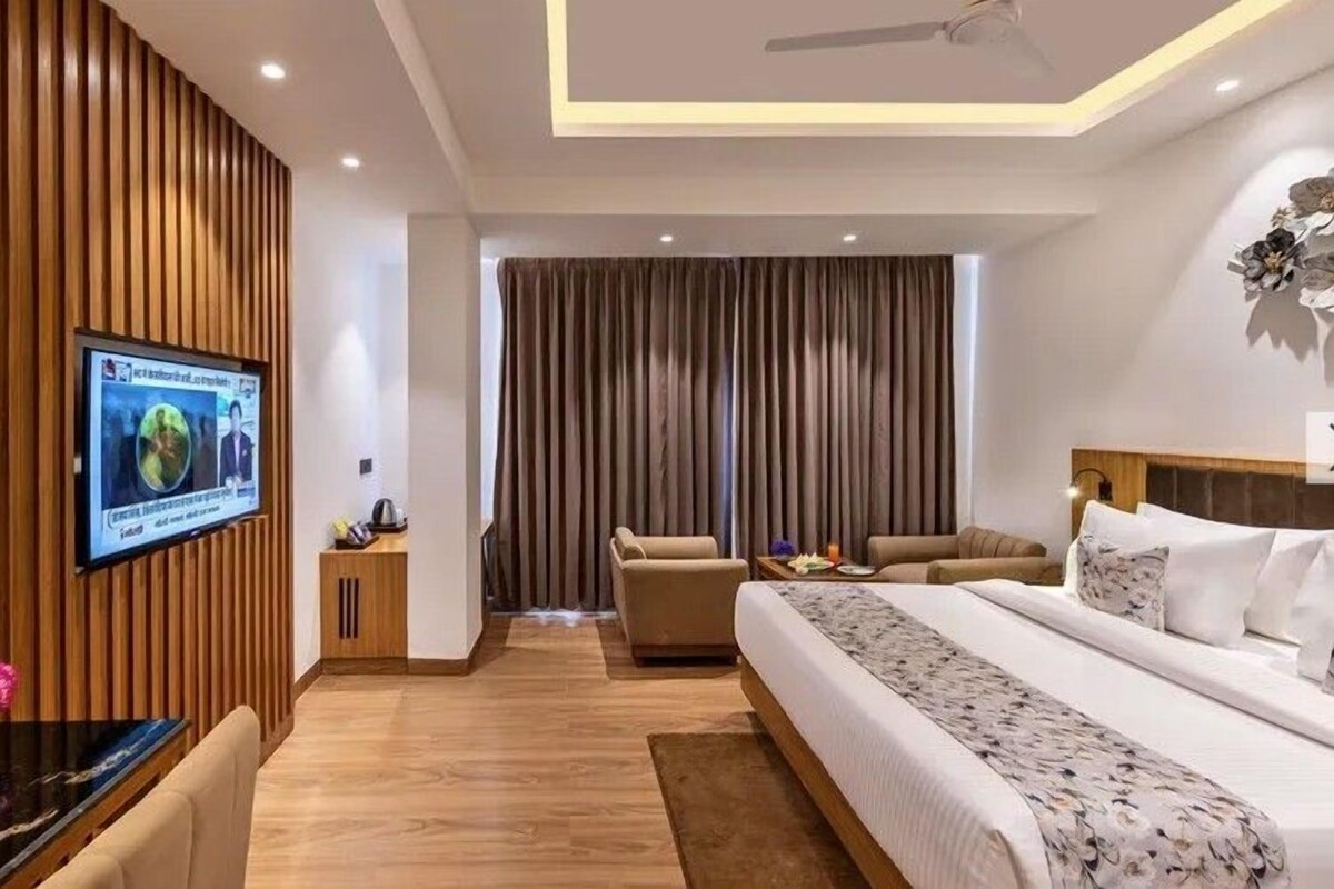 Une chambre d’hôtel moderne dotée d’un grand lit, d’un bureau avec un téléviseur à écran plat, d’un canapé et d’une grande fenêtre avec des rideaux.