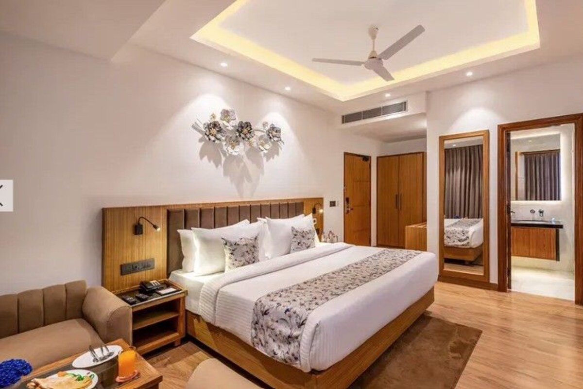 A modern hotel room with a large bed, wooden headboard, bedside tables, a desk, and a chair.