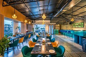 A modern restaurant with a long dining area, multiple tables, and chairs. There is a bar area with a counter and stools. The ceiling has a metal grid design, and there are hanging lights. - Lords Eco Inn Dehradun (Dehradun)