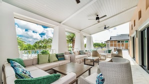 Ein großzügiger Außenbereich mit einer Couch, Sesseln und einem Tisch, mit Blick auf einen Pool und Palmen.