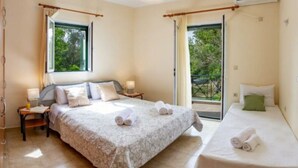 Ein Hotelzimmer mit einem großen Bett, einem kleineren Bett, einem Nachttisch, einer Lampe und einem Fenster mit Vorhängen.