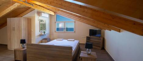 A bedroom with a wooden ceiling, a bed, bedside tables, a TV, and a window with a view.