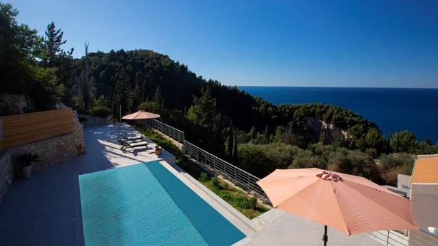 Zona de piscina con sillones de playa y sombrillas, con vistas al paisaje costero.