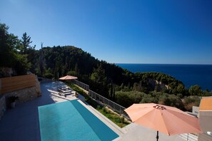 A pool area with lounge chairs and umbrellas overlooking a coastal landscape. - Kathisma Sunset Villlas (Lefkada)