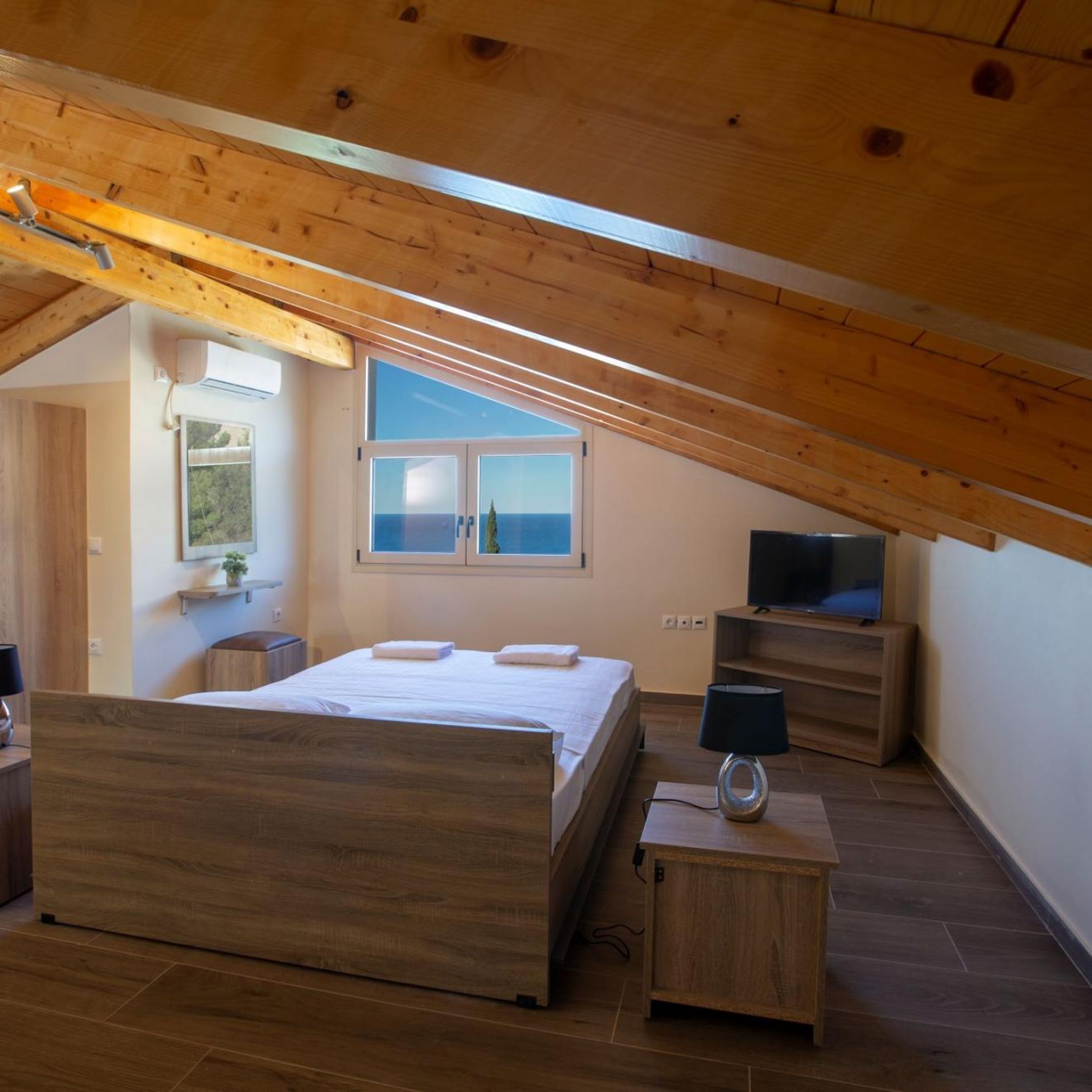 A bedroom with a wooden ceiling, a bed, a TV, and a window with a view.