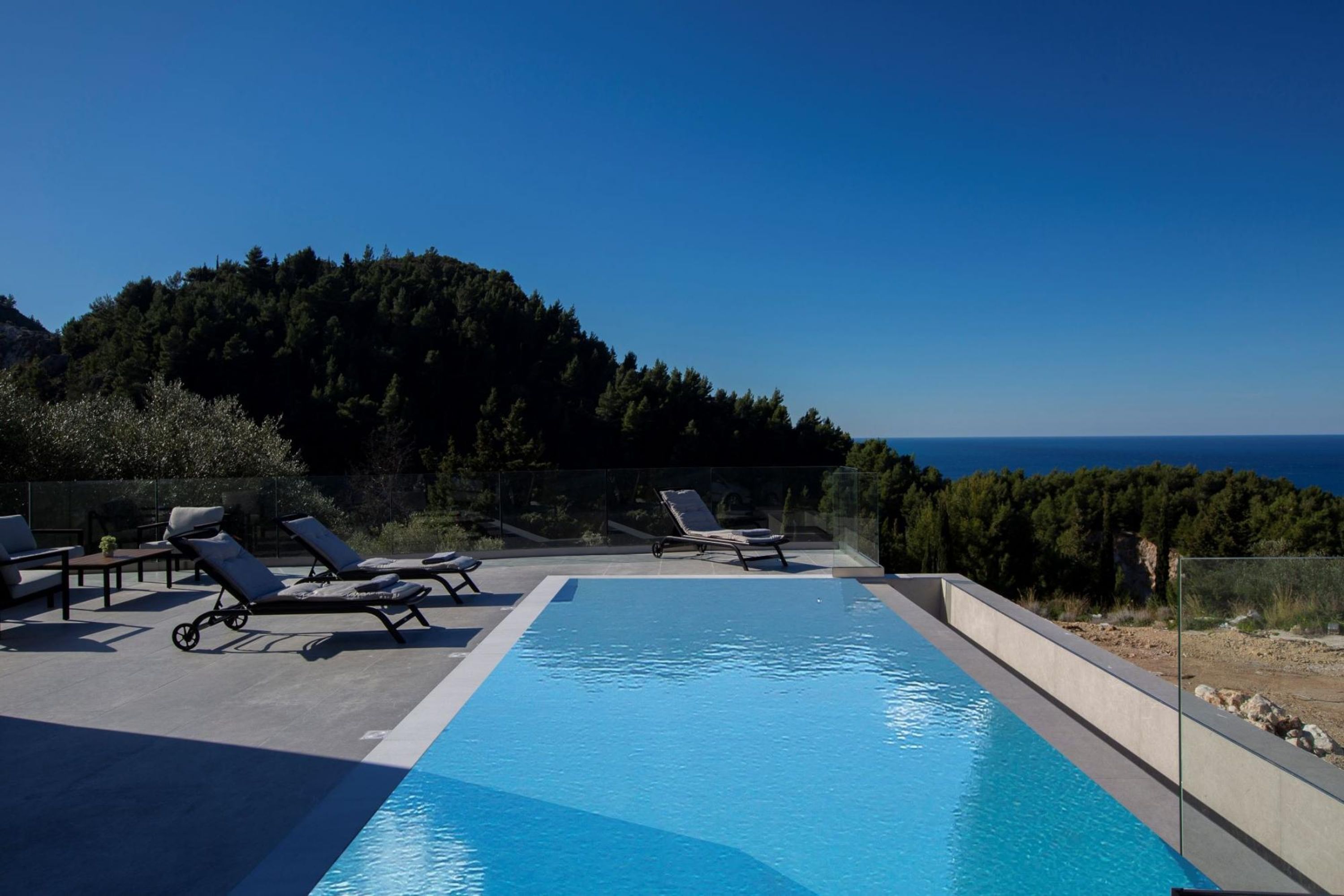 Una piscina con sillones de descanso y vista al mar.