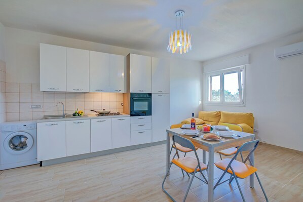 A modern kitchen with white cabinets, a washing machine, and a dining area with a table and chairs. - Le Bianche Apt 2 with Garden near The Sea (Manduria)