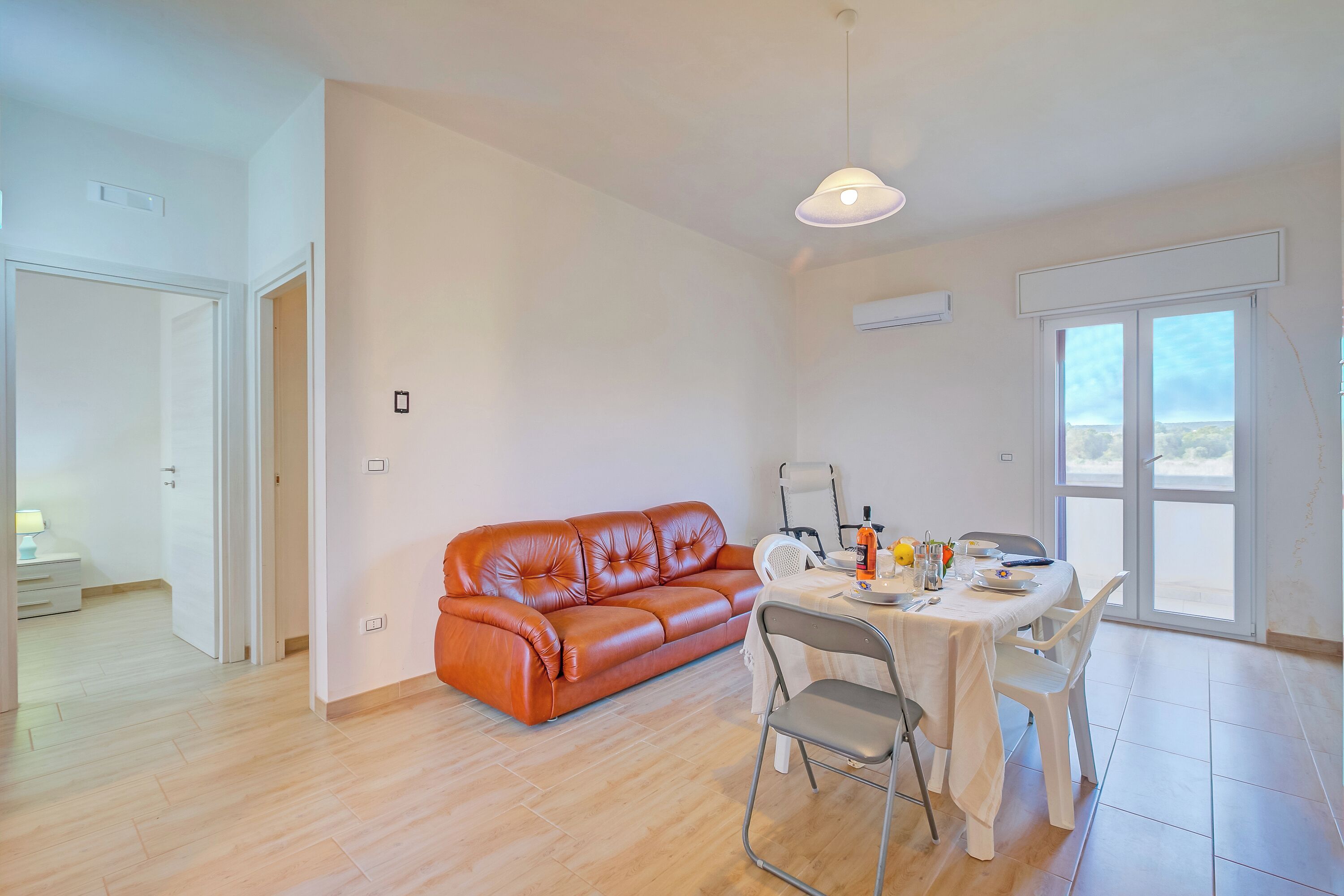 A modern living room with a leather sofa, a dining table with chairs, and a large window providing a view.