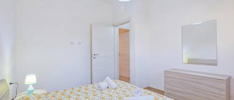 Une chambre à coucher comprenant un lit, une lampe de chevet, une commode, un miroir et une porte donnant sur une autre pièce.