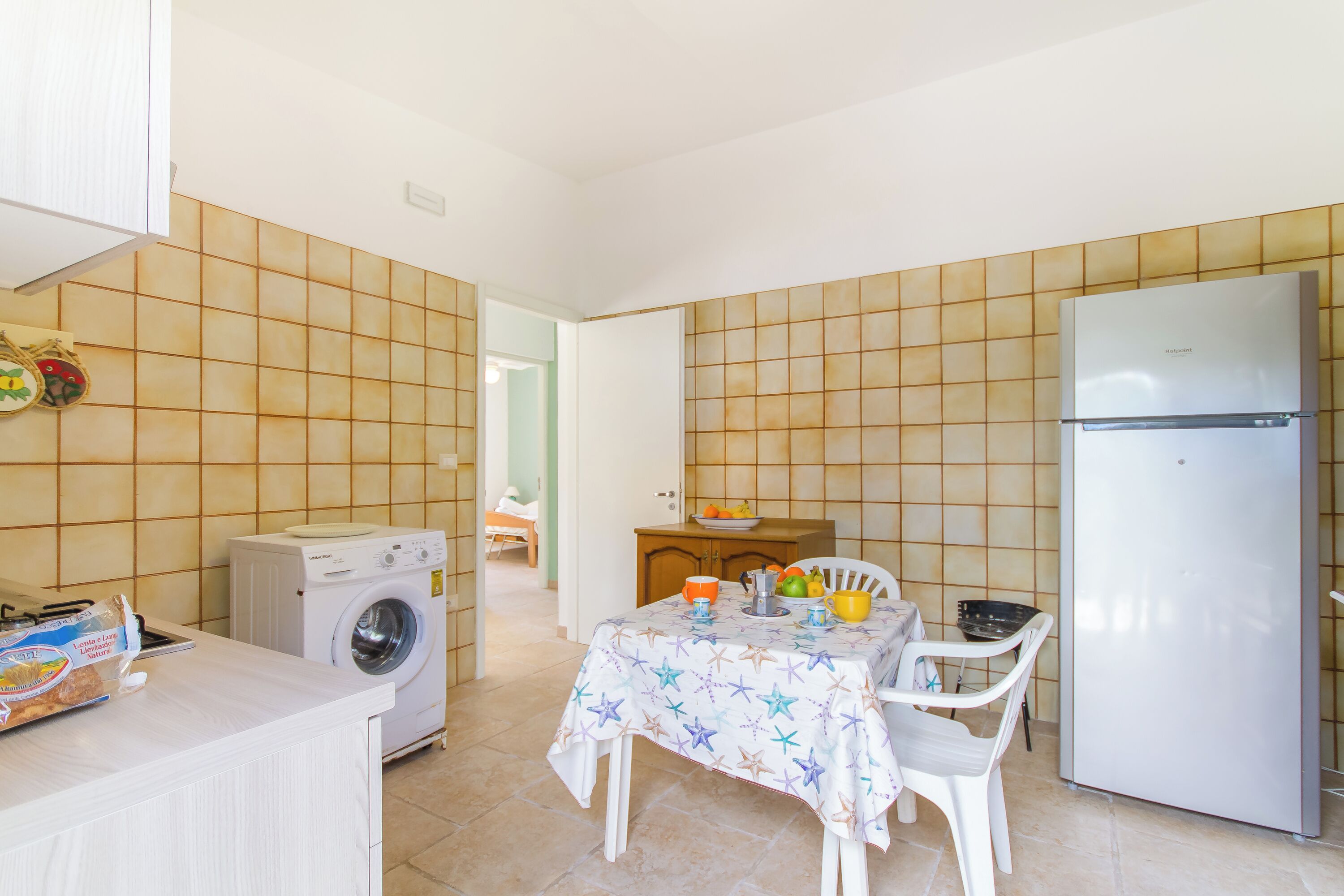 Una cocina compacta con lavadora, refrigerador, una mesa de comedor con sillas y un salpicadero de azulejos.