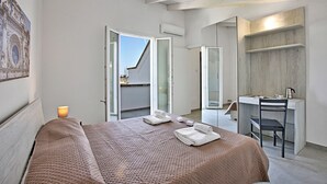 Une chambre à coucher avec un lit, un bureau et une chaise. Il y a une fenêtre et un appareil de climatisation.
