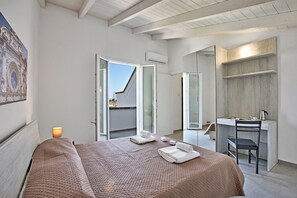 Une chambre à coucher avec un lit, un bureau et une chaise. Il y a une fenêtre et un appareil de climatisation.