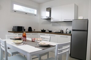 Una cocina moderna con armarios blancos, un refrigerador de acero inoxidable y una mesa de comedor preparada para cuatro comensales.