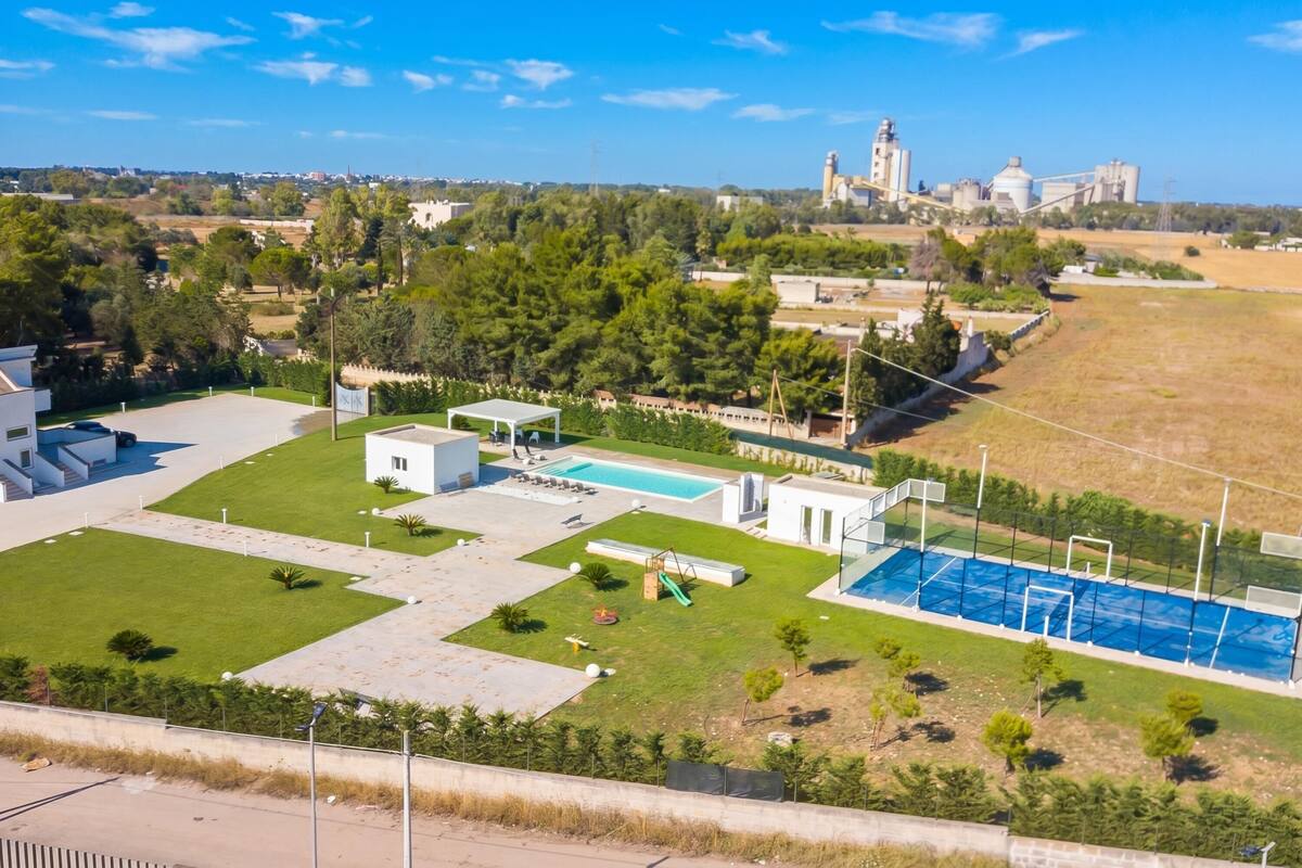 Un quartier résidentiel avec une piscine, un petit bâtiment et, au loin, un grand complexe industriel.