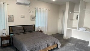 A bedroom with a bed, bedside tables, a wall-mounted air conditioner, and a built-in shelving unit. - Bri's On The Beach (Treasure Beach)