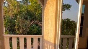 A covered outdoor area with a concrete floor, white railings, and a glass door leading to an interior space. - Bri's On The Beach (Treasure Beach)