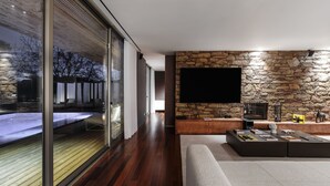 A modern living room with a stone wall, a flat-screen TV, and a wooden floor. - Golf Villa - Heated Pool Golf Course (Ponte de Lima)
