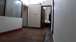 A narrow hallway with a tiled floor, a door on the right, and a window on the left. - HOTEL BHUBANESWAR PRIDE (Bhubaneshwar)