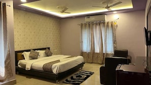 A bedroom with a bed, a desk, a chair, a ceiling fan, and an air conditioning unit. - HOTEL BHUBANESWAR PRIDE (Bhubaneshwar)