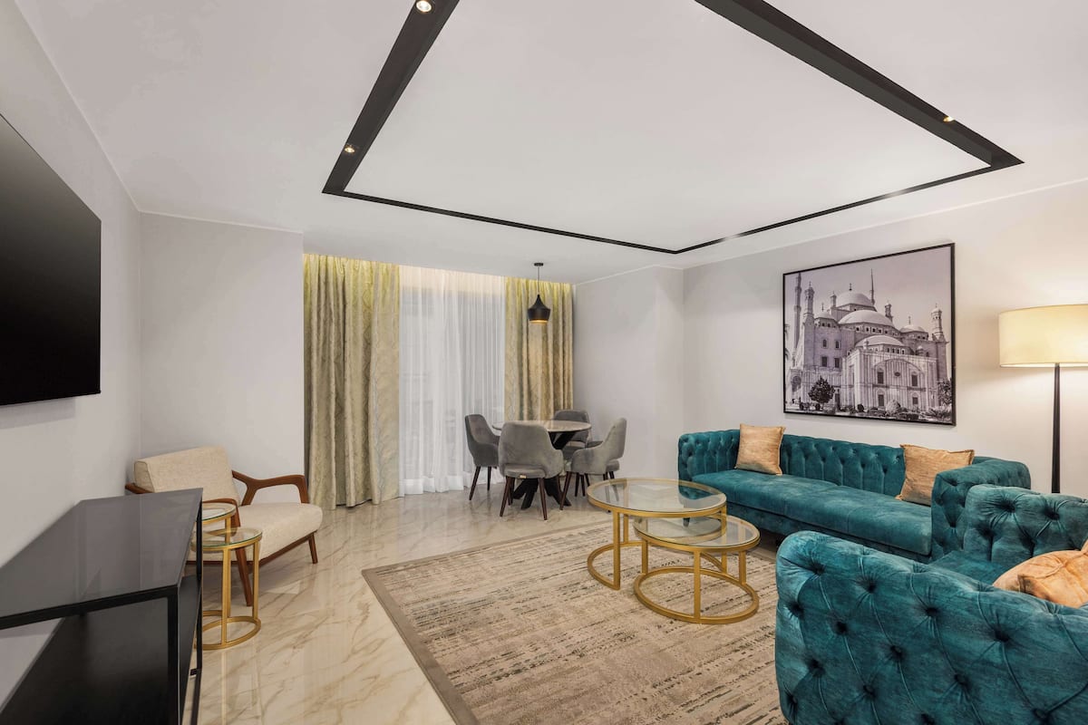 Una sala de estar moderna con un sofá verde azulado, una mesa de centro de vidrio, un televisor y un comedor con sillas y una mesa.