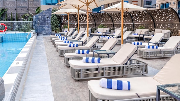A poolside area with lounge chairs and umbrellas, a pool, and a modern building facade. - Radisson Residences Cairo Heliopolis (Cairo)