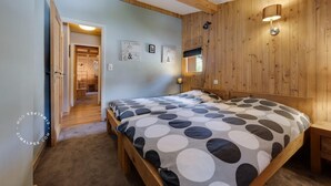 Une chambre avec un plafond en bois, un lit recouvert d’une housse à motifs à pois, une table de chevet en bois et une lampe fixée au mur.