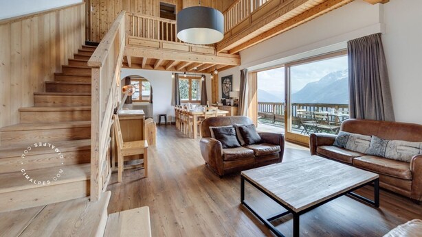 Un vaste espace de vie agrémenté d’un escalier en bois, de canapés en cuir et d’une grande fenêtre offrant une vue sur les montagnes.