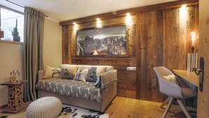 A cozy room with a wooden wall, a mounted painting, a sofa, a chair, and a small table with glasses. - Apartment Aschbach - cosy for couples or families with 1-2 children  (Kitzbuhel)