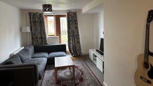 A living room with a sofa, a coffee table, a TV stand, and a guitar. - Immaculate 2-bed Apartment in Greenhithe (Greenhithe)