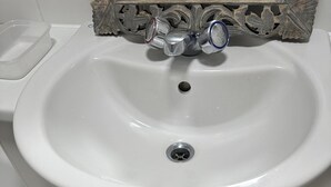 A bathroom with a white sink, a drain, and a small vent. There is a striped rug and a pair of black slippers on the floor. - Immaculate 2-bed Apartment in Greenhithe (Greenhithe)