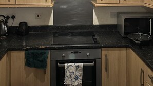 A kitchen with wooden cabinets, a stove, a microwave, and a ceiling light. - Immaculate 2-bed Apartment in Greenhithe (Greenhithe)