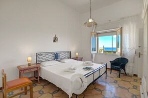 Quarto com cama, mesas de cabeceira, cadeira, janela com vista e luminária suspensa.