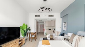 Una sala de estar moderna con un televisor de pantalla plana, mueble de entretenimiento de madera, comedor y una cocina al fondo.
