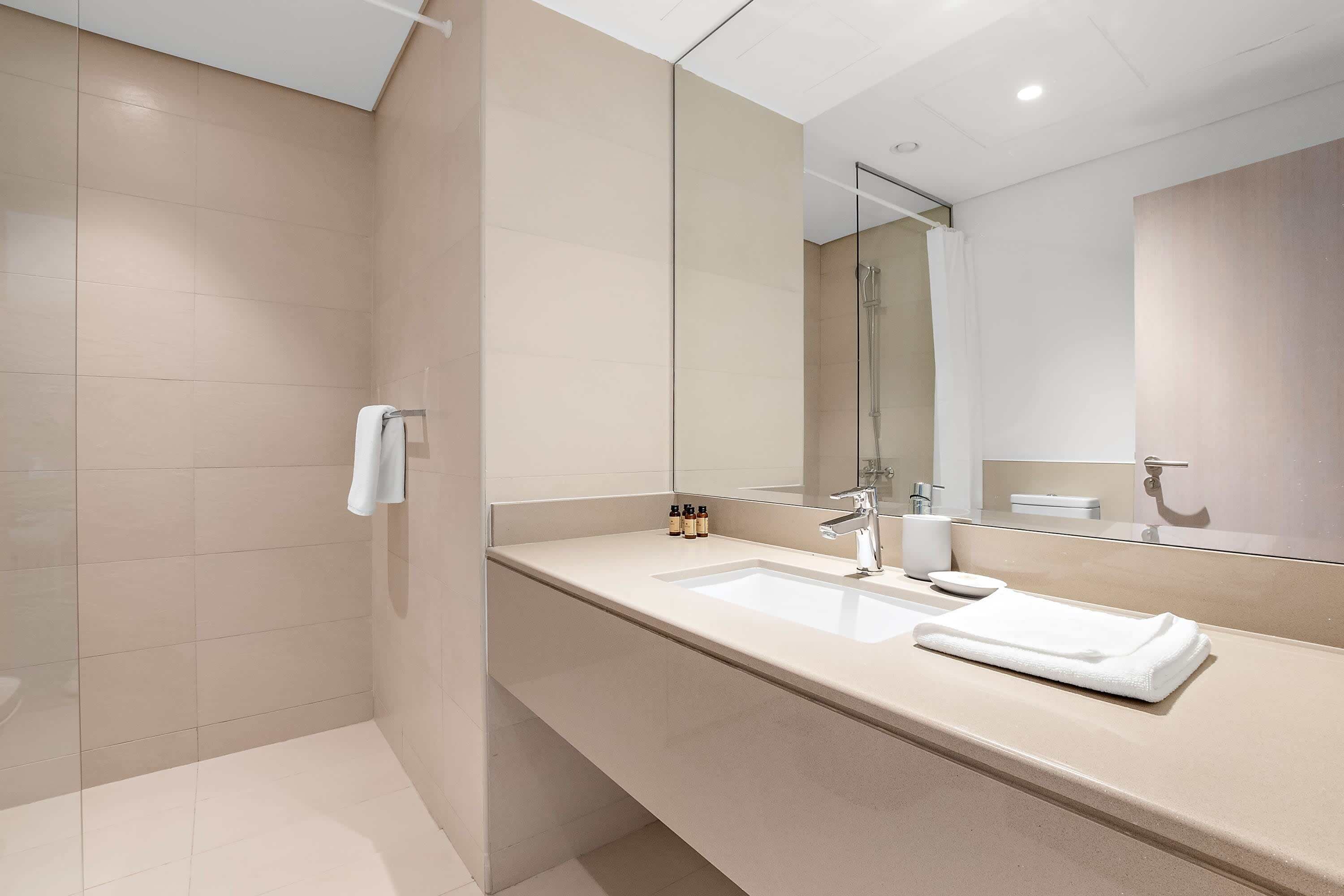 A modern bathroom with a large mirror, a sink, and a shower area.