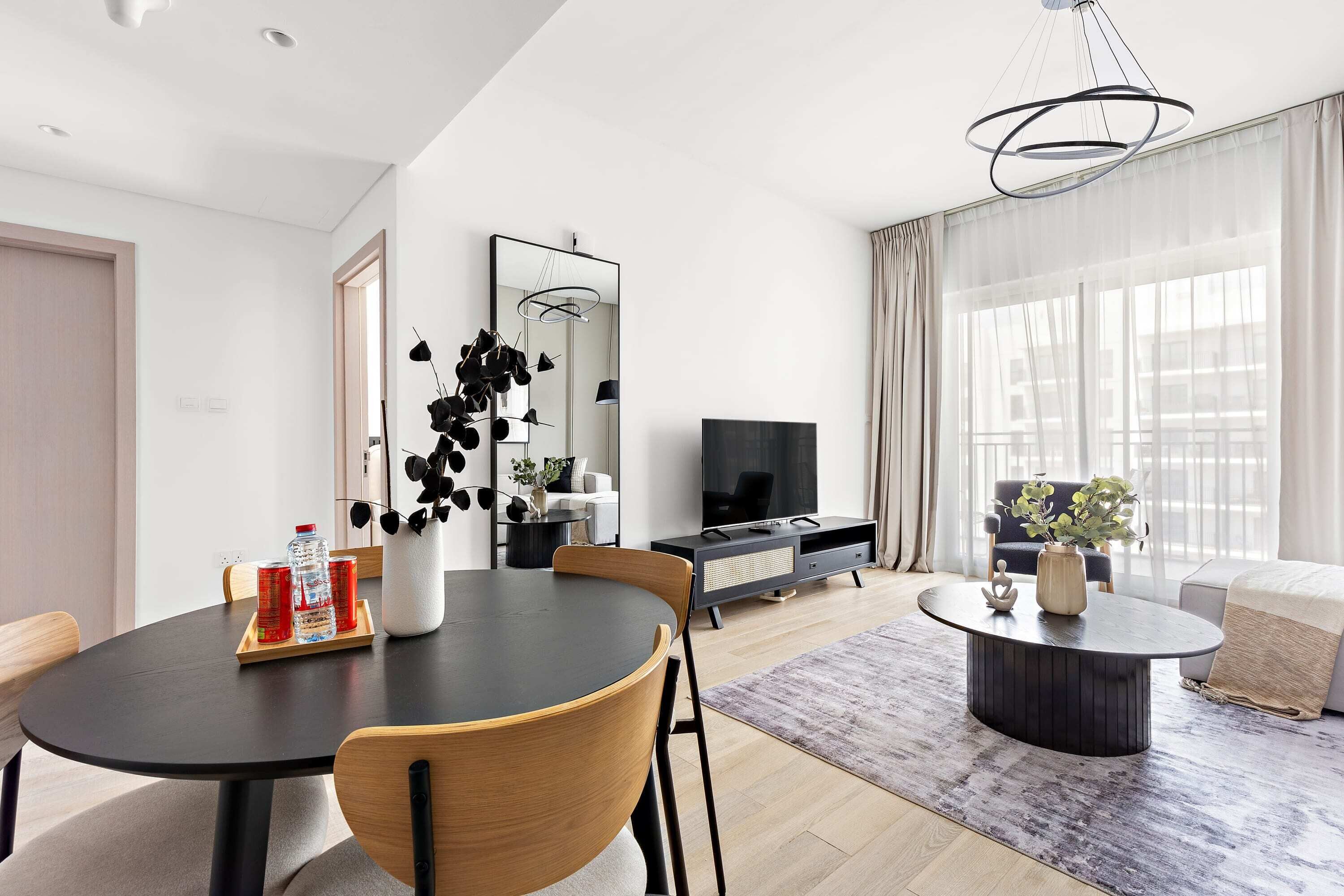 Un salon moderne avec une table à manger ronde, un canapé, un téléviseur et une grande fenêtre avec des rideaux.