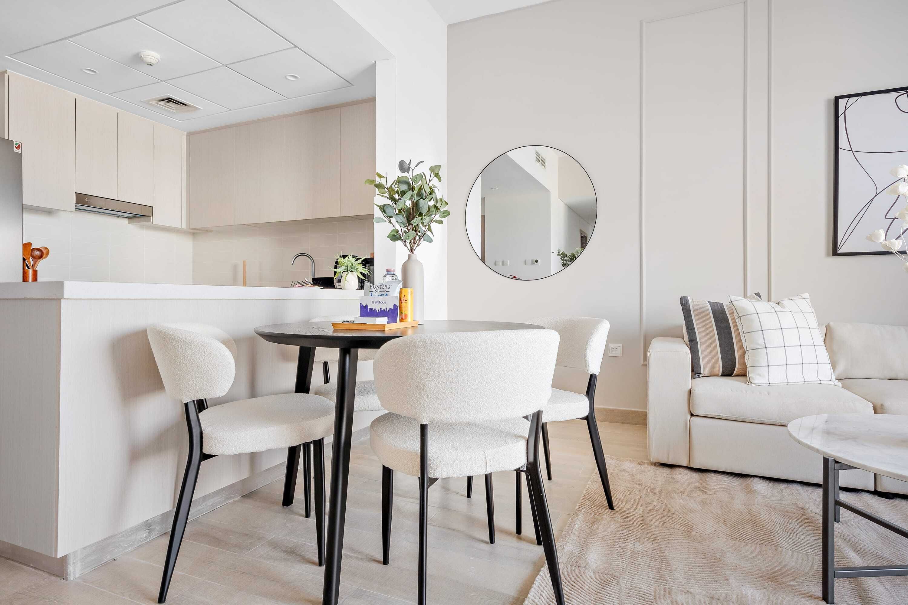 A modern kitchen with white cabinets, a round mirror, and a dining area with white chairs and a table.