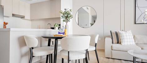 A modern kitchen with white cabinets, a round mirror, and a dining area with white chairs and a table.