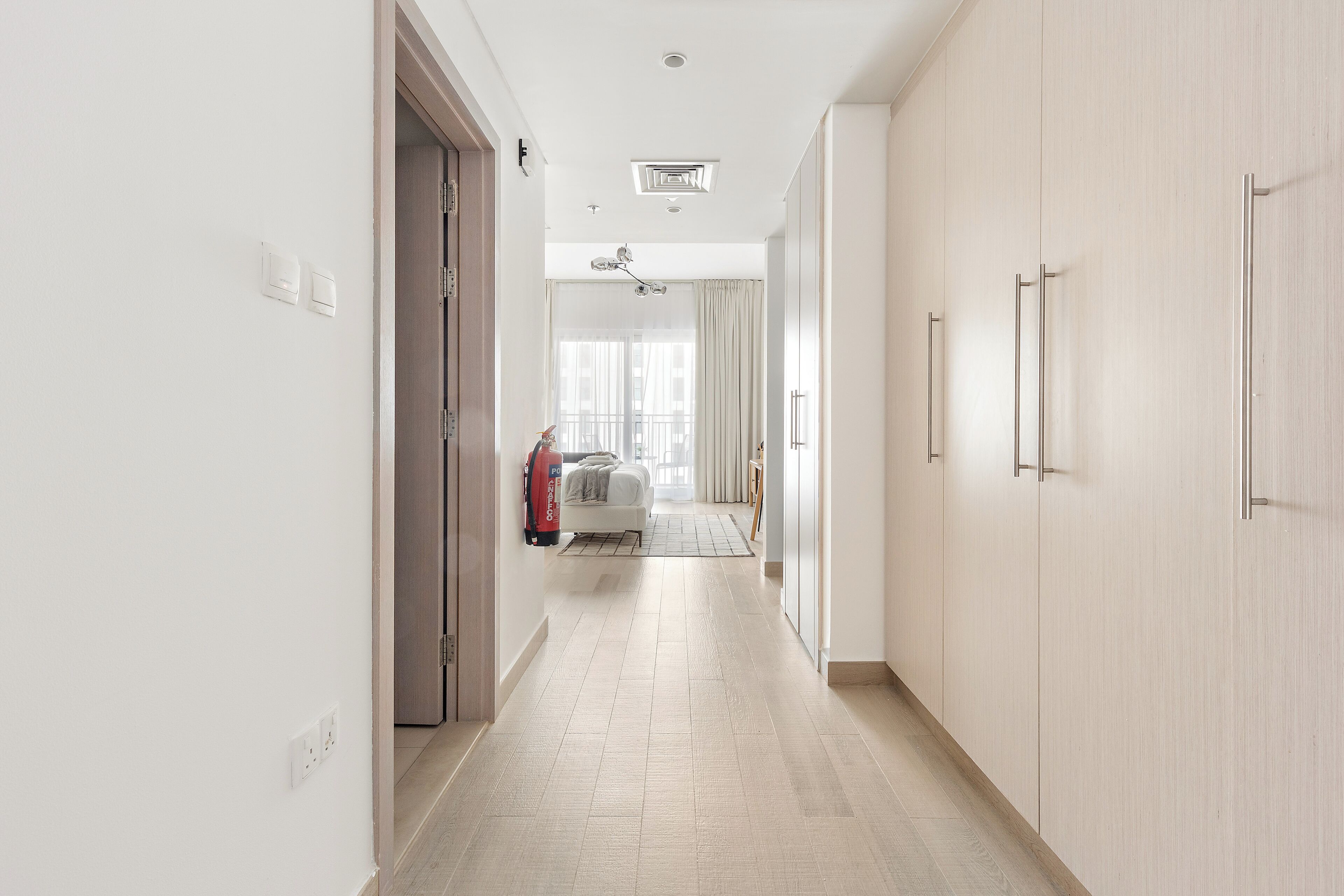 A hallway with a light-colored floor, white walls, and a door on the left.
