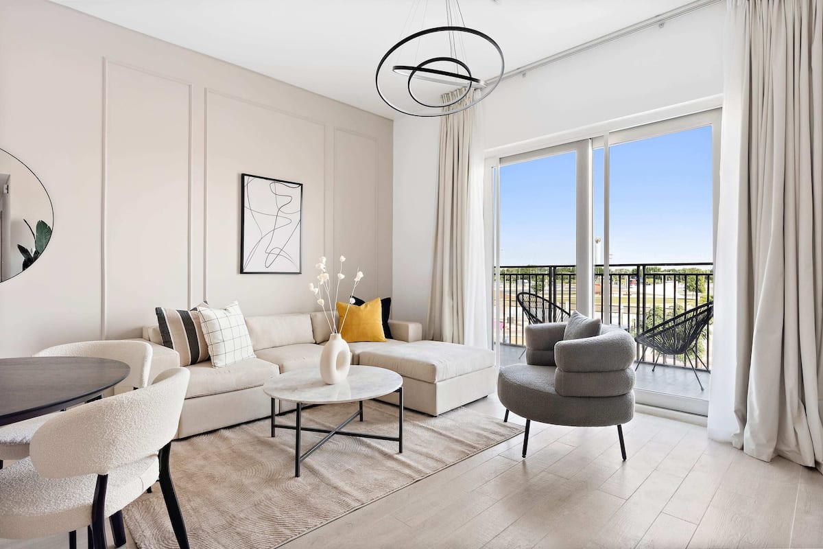 Una sala moderna con un sofá, sillones, una mesa de centro y un comedor. Hay un balcón con vistas al exterior.