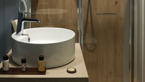 Une salle de bain moderne avec un lavabo rond, une douchette à main et une douche à parois de verre.