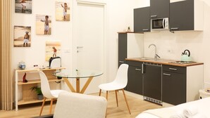 Une cuisine compacte équipée d’un four à micro-ondes, d’un évier et d’un petit plan de travail. Un coin repas est aménagé avec une table en verre et des chaises blanches.